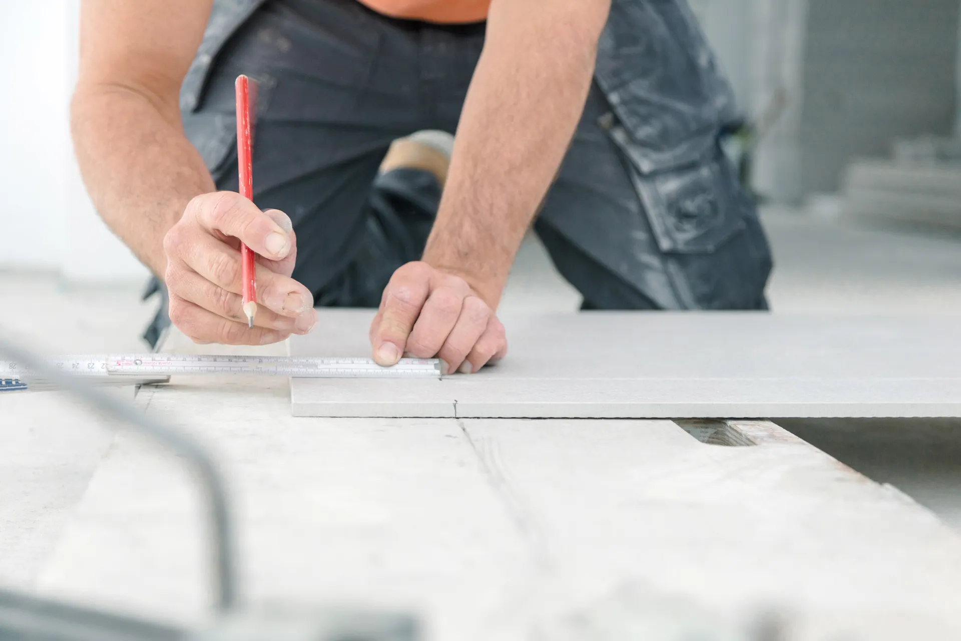 Handwerker zeichnet mit Bleistift ein Maß auf eine Fliese
