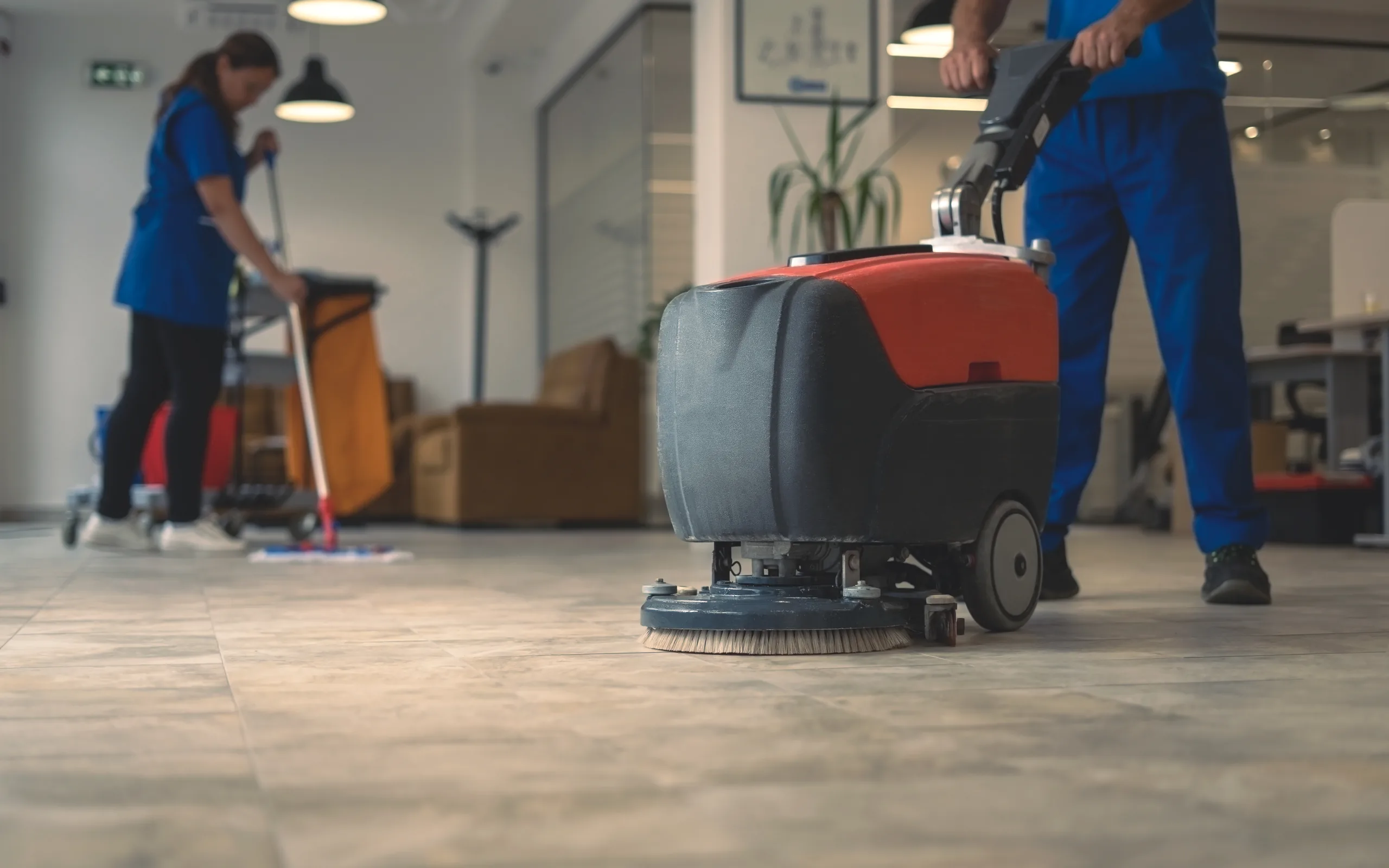 Reinigungskräfte reinigen den Boden eines Büros mit Scheuersaugmaschine und Wischmopp