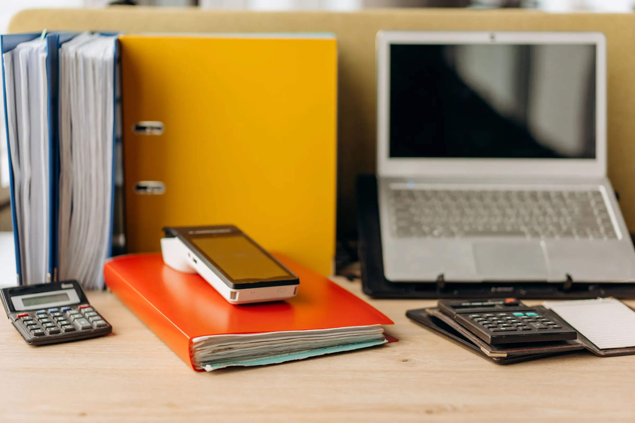 Schreibtisch mit Aktenordnern, zwei Taschenrechnern, Kartenterminal und Laptop