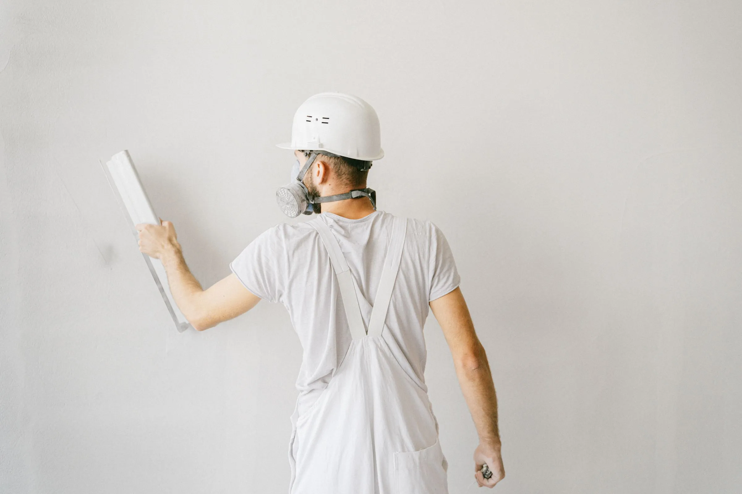 Handwerker mit Helm und Atemschutz von hinten beim Glätten einer Wand