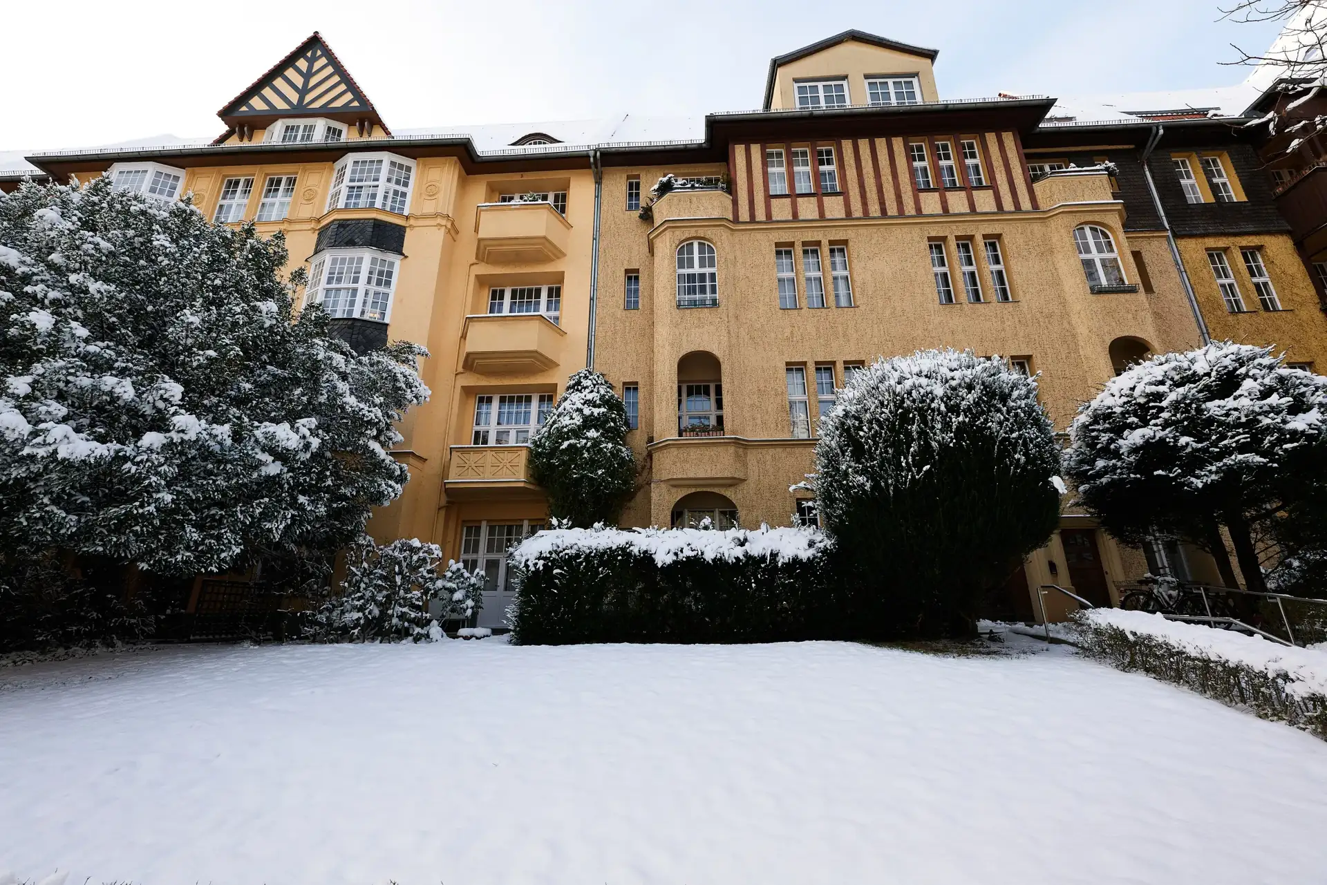 Mehrfamilienhaus mit verschneitem Vorgarten und Hecken im Winter